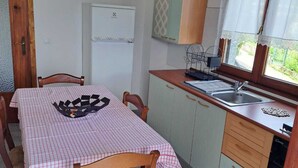 A compact kitchen with a dining table, chairs, a refrigerator, a sink, and a window with curtains. - RED FOUNTAIN HOUSE 2 (arizzano)