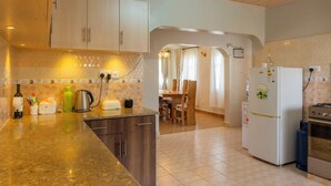 A kitchen with wooden cabinets, a granite countertop, a refrigerator, a stove, and a dining area with a table and chairs. - Gatundu Peaceful Tea Farm Stay w/activities (Gatundu)
