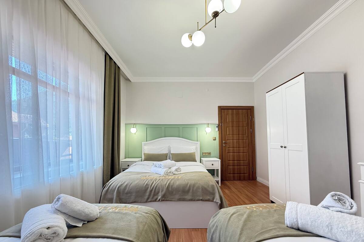 A hotel room with two beds, a wardrobe, a nightstand, and a window with curtains.