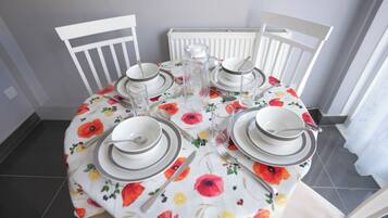 A dining table set with plates, bowls, and cutlery, surrounded by white chairs.