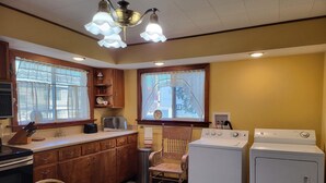 A compact kitchen with wooden cabinets, a dining table with a bowl, a stove, and a washing machine.