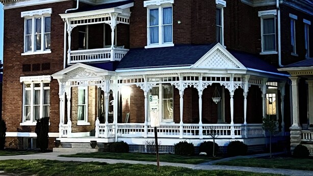 A large, two-story brick house with a wrap-around porch and a second-story balcony.