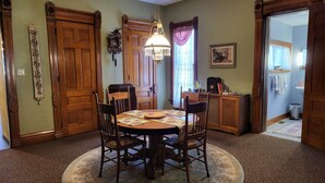 A dining room with a wooden table, four chairs, a chandelier, and a clock on the wall.