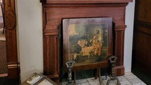 A room with a large mirror above a fireplace, a framed painting below, and a small table with a tray.