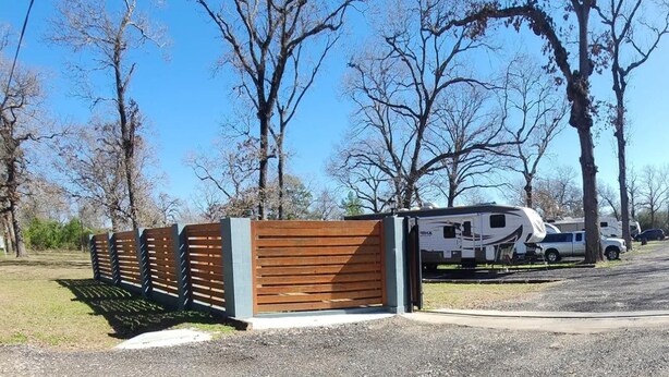 A gated RV park with a white RV and a truck parked inside. - Serene Pinehurst Camper - Sleeps 2 - Pet Friendly (Magnolia)