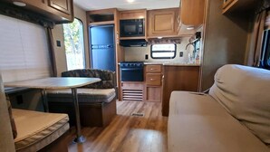 A compact RV kitchen with a stove, microwave, and refrigerator. - Serene Pinehurst Camper - Sleeps 2 - Pet Friendly (Magnolia)