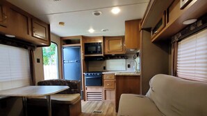 A compact RV interior with a kitchenette, a dining area, and a seating space. - Serene Pinehurst Camper - Sleeps 2 - Pet Friendly (Magnolia)