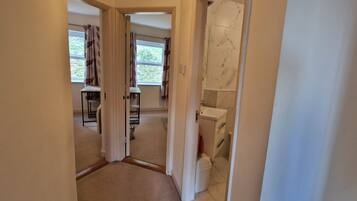A narrow hallway with a view into a room that includes a toilet, a window with curtains, and a small table.