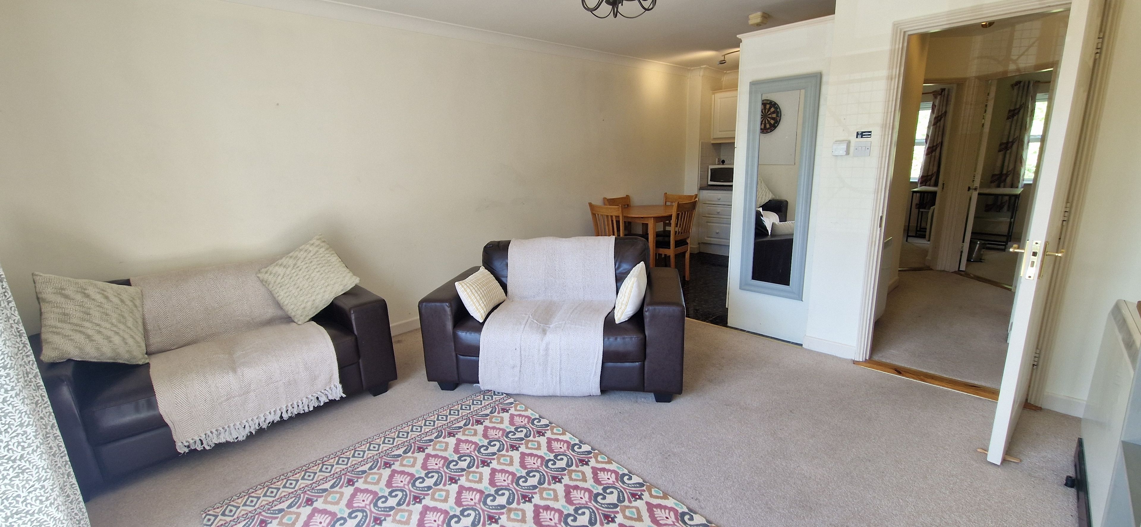 A living room with two sofas, a patterned rug, and a dining area with a table and chairs.
