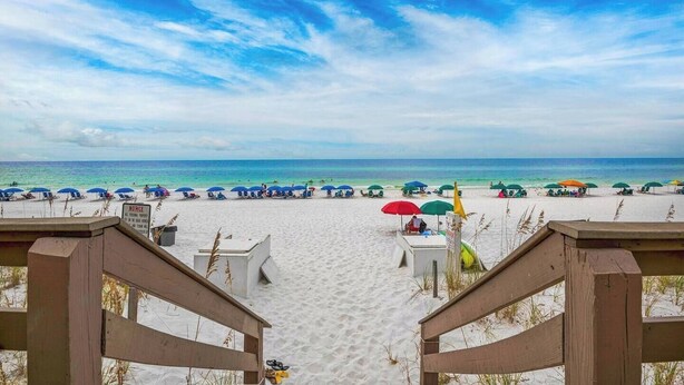 A beach with white sand, blue sky, and a view of the ocean. There are beach umbrellas and chairs. - Nautilus 2511 Gulf View 2 BR/2 BA 5th Floor 2026 REMODEL! (FORT WALTON BEACH)
