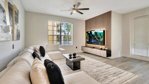 Una sala de estar moderna con un sofá blanco, una mesa de centro y un televisor de pantalla plana montado en una pared de paneles de madera.