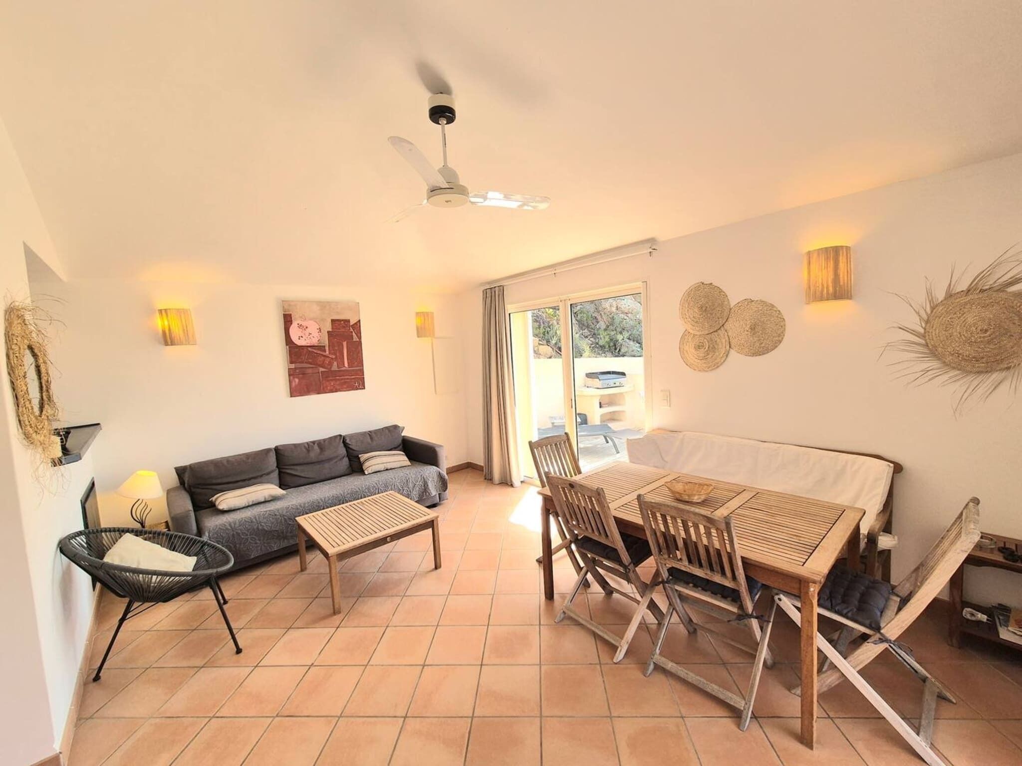 Uma sala ampla com sofá, mesa de jantar com cadeiras, ventilador de teto e vista para área externa através de uma porta de vidro.