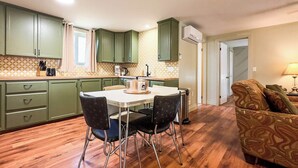 Una cocina compacta con armarios verdes, una mesa de comedor con cuatro sillas y una estufa empotrada.