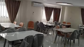 Ein Hotelrestaurant mit Tischen, Stühlen, Klimaanlagen und Vorhängen.