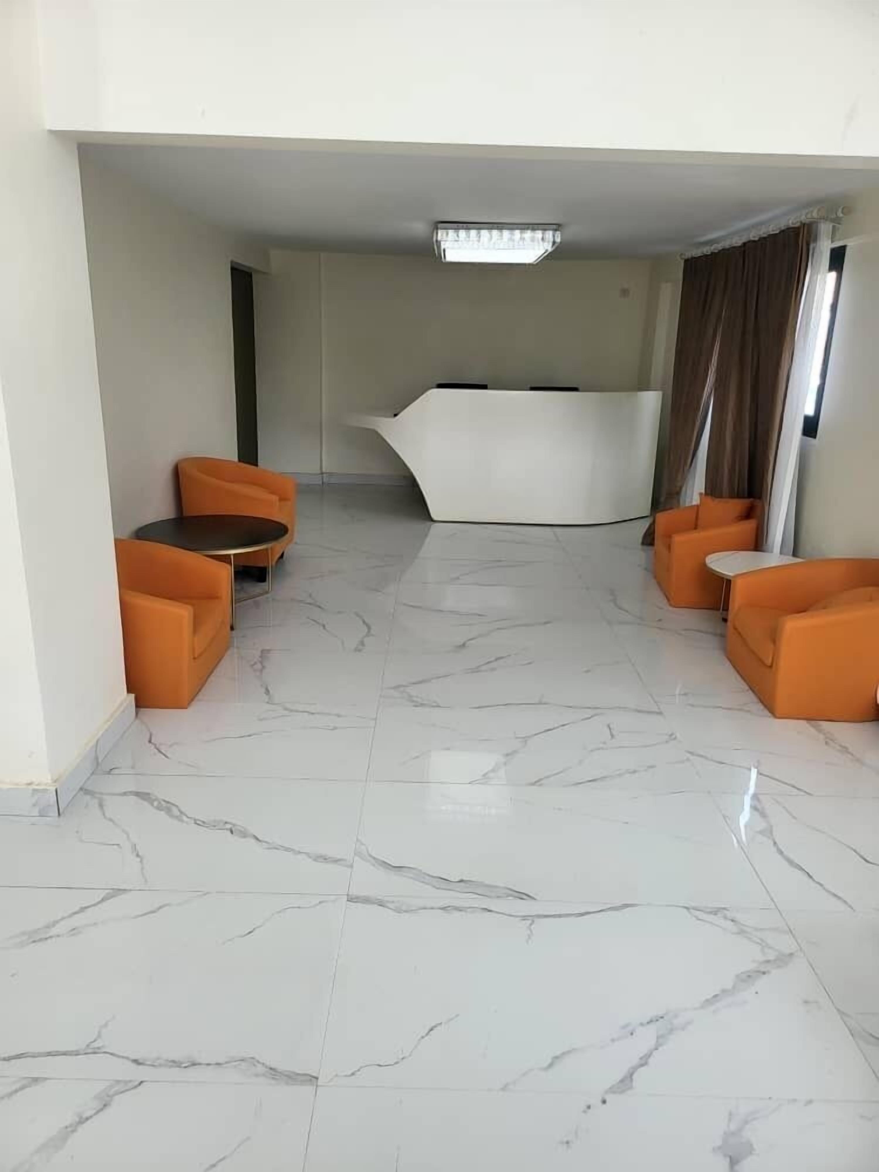 A modern room with a marble floor, two orange armchairs, a small round table, and a white sofa.