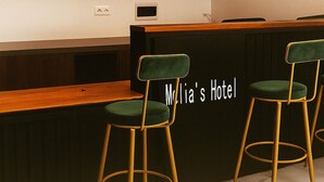 A reception desk with a sign reading "Mr. Lia's Hotel" and two green upholstered bar stools with gold legs. - Melia's Hôtel Diamniadio  (Diamniadio)