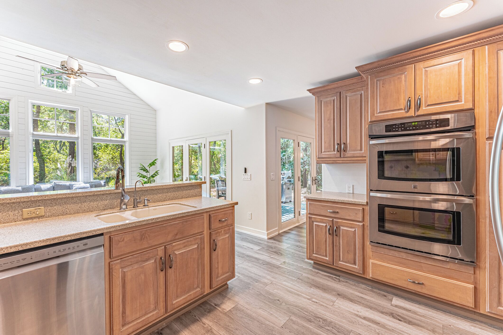 A modern kitchen with wooden cabinets, stainless steel appliances, and a large window overlooking a backyard.