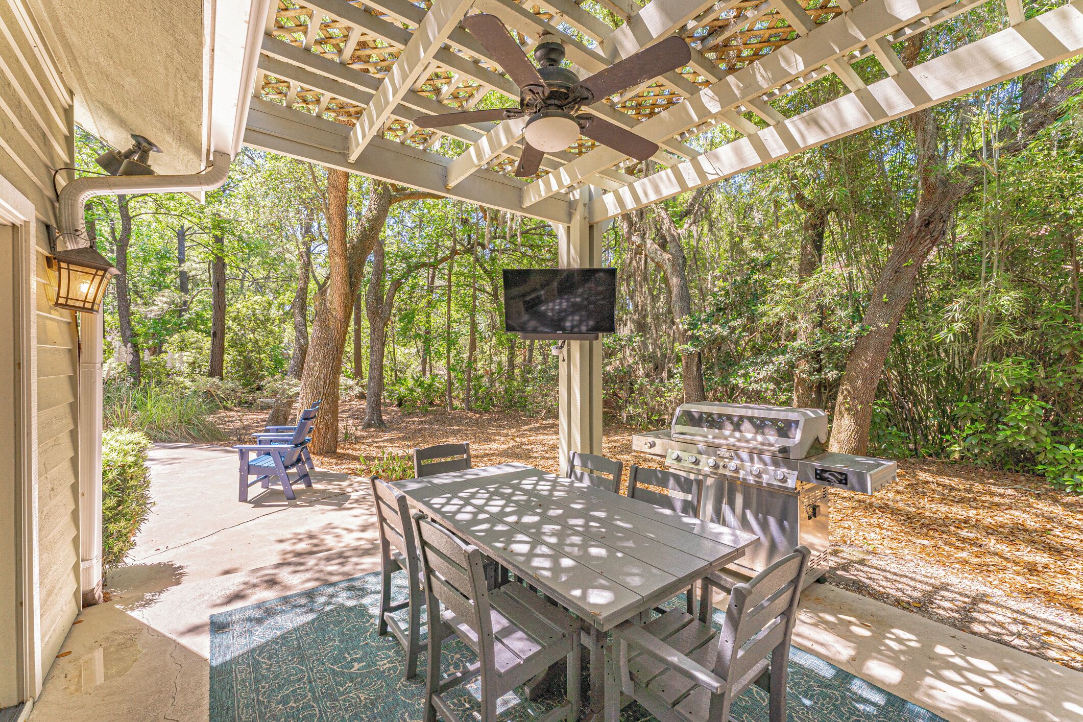 Une terrasse extérieure avec une table et des chaises, un ventilateur de plafond, un téléviseur et un barbecue.