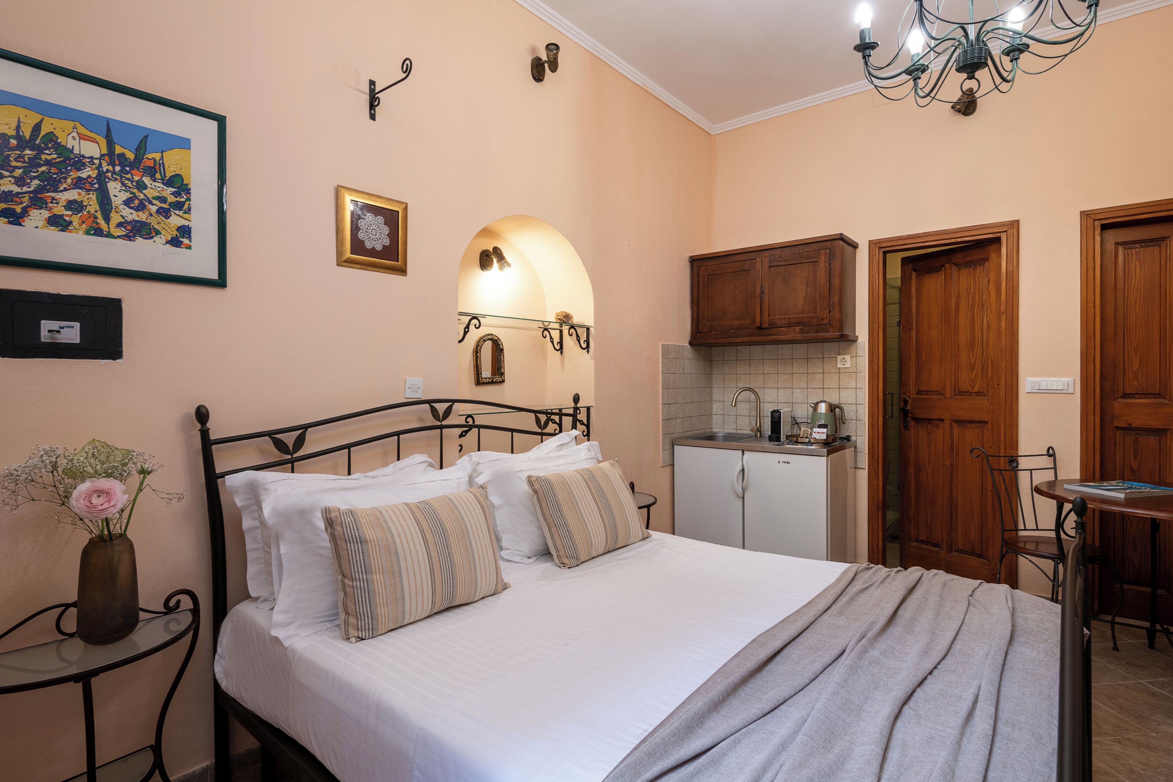 Un dormitorio con una cama, una mesita de noche con un florero, un espejo en la pared y una kitchenette.