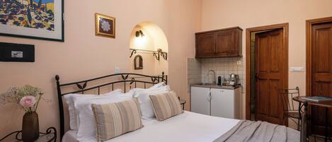Un dormitorio con una cama, una mesita de noche con un florero, un espejo en la pared y una kitchenette.
