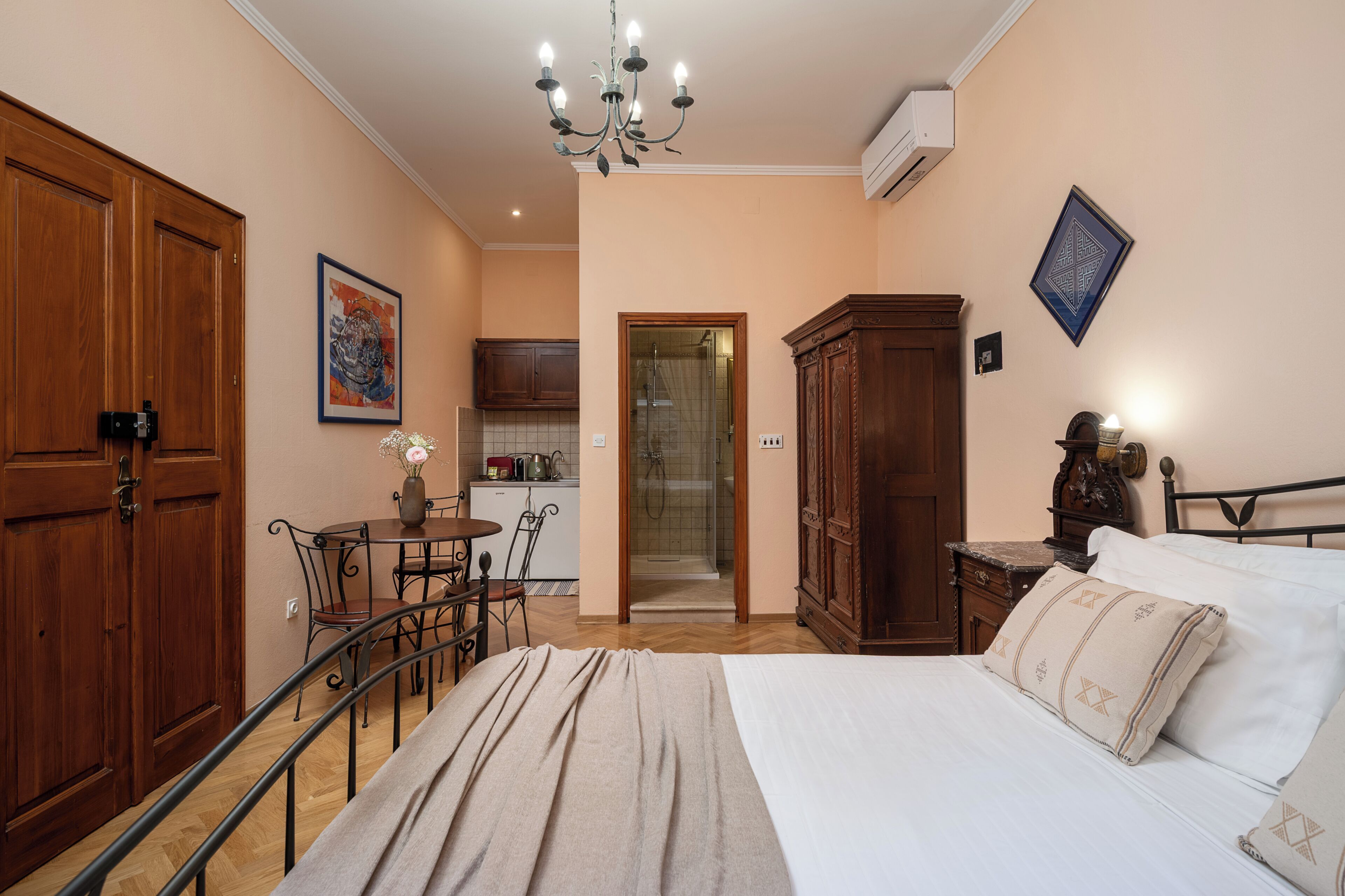Een slaapkamer met een bed, een houten garderobe, een bureau met stoel en een klein keukenhoekje.