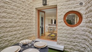 A dining area with a table set for four, a glass door leading to a dining room, and a round mirror on the wall.