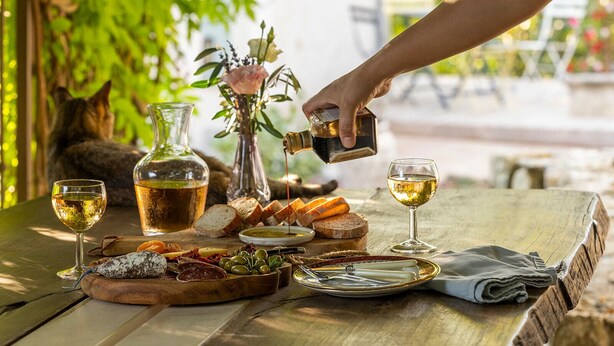 A table set with a bottle of olive oil, two glasses of wine, bread, cheese, and olives.
