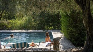 A pool area with a stone wall, lounge chairs, and a table with a drink.