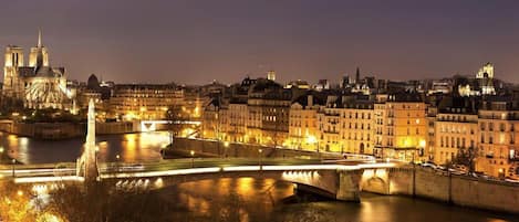 A nighttime cityscape with a prominent cathedral and a bridge over a river.