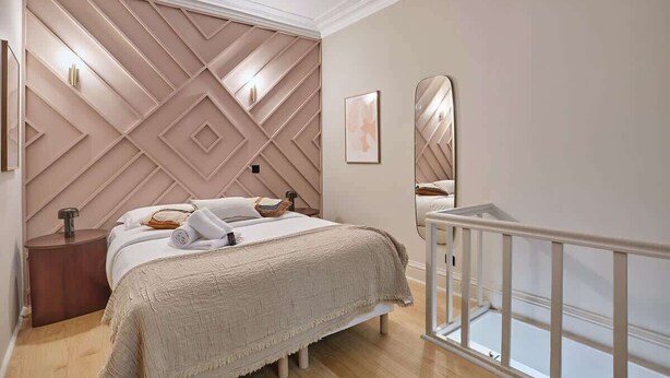 Un dormitorio con cama, mesita de noche, espejo y barandilla blanca.