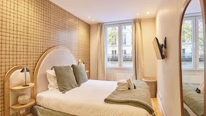 Un dormitorio con una cama grande, una mesita de noche, una lámpara, un espejo y una ventana con cortinas.