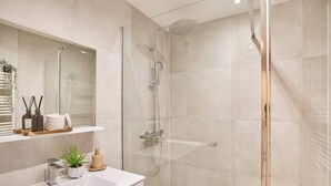 Un baño moderno con ducha de vidrio, lavamanos blanco y espejo sobre él.