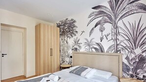 A bedroom with a large bed, a wardrobe, a small round table, and a mural of tropical plants. - Elegant and modern apartment  Eiffel Tower (Paris)