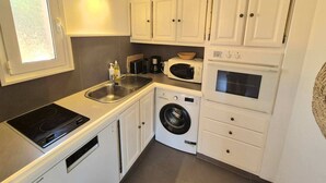 Una cocina compacta con armarios blancos, un microondas integrado, una lavadora y una estufa.