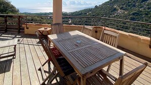 A wooden deck with a table and chairs, overlooking a mountainous landscape.