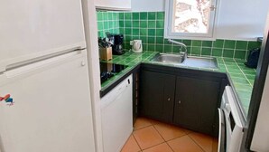 A compact kitchen with a white refrigerator, a dishwasher, a sink, and a window above it.