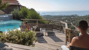 A wooden deck with a pool, overlooking a coastal landscape.