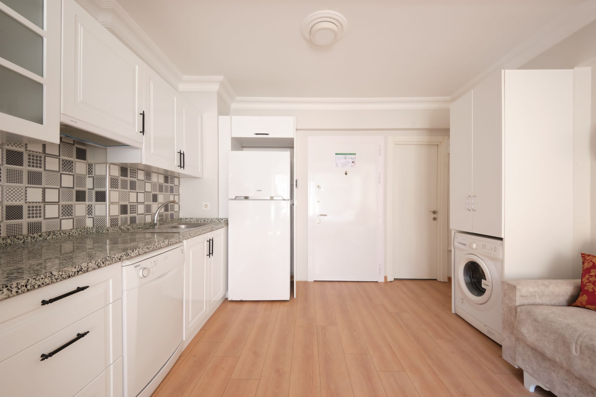 A modern kitchen with white cabinetry, a granite countertop, and a built-in washing machine.
