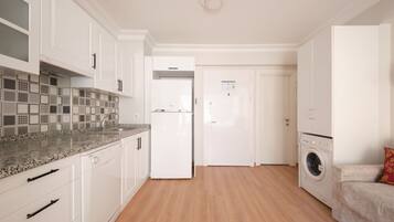 A modern kitchen with white cabinetry, a granite countertop, and a built-in washing machine.
