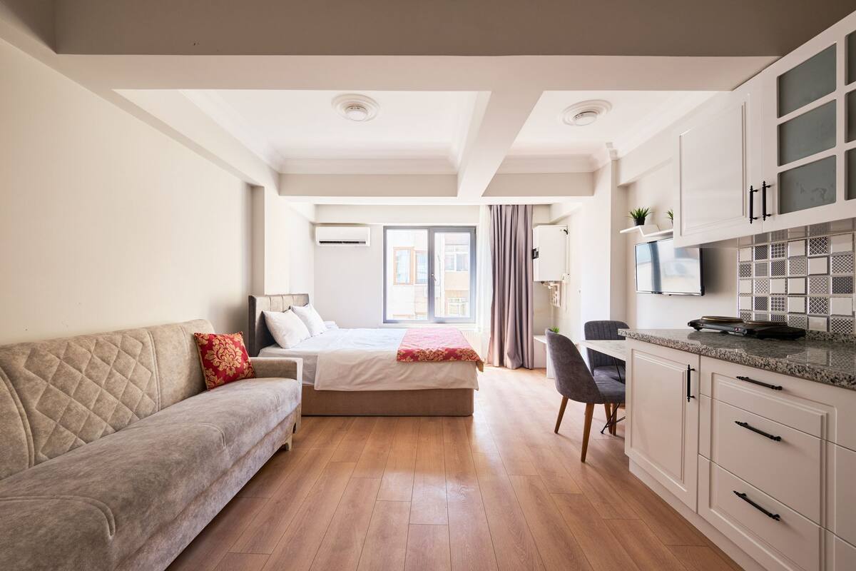 A modern, well-lit bedroom with a bed, a sofa, and a desk area.