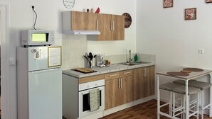 Une cuisine moderne avec un réfrigérateur, un four à micro-ondes et un four, tous de couleur blanche. On y trouve un meuble en bois, au-dessus duquel est suspendu un luminaire.
