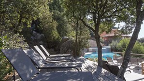 A wooden deck with lounge chairs overlooking a pool, surrounded by trees and rocks.
