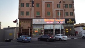 A hotel with multiple floors, a signboard with the hotel's name, and several storefronts including a chocolate shop and a bakery. - MASSET ALMASEM5 SERVICED APARTMENTS (Al-Hofuf)