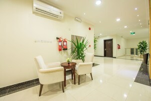 A hotel lobby with a reception desk, two chairs, a potted plant, and a fire extinguisher.