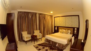 A hotel room with a large bed, two armchairs, a small table, a TV, and a large mirror. - MASSET ALMASEM5 SERVICED APARTMENTS (Al-Hofuf)