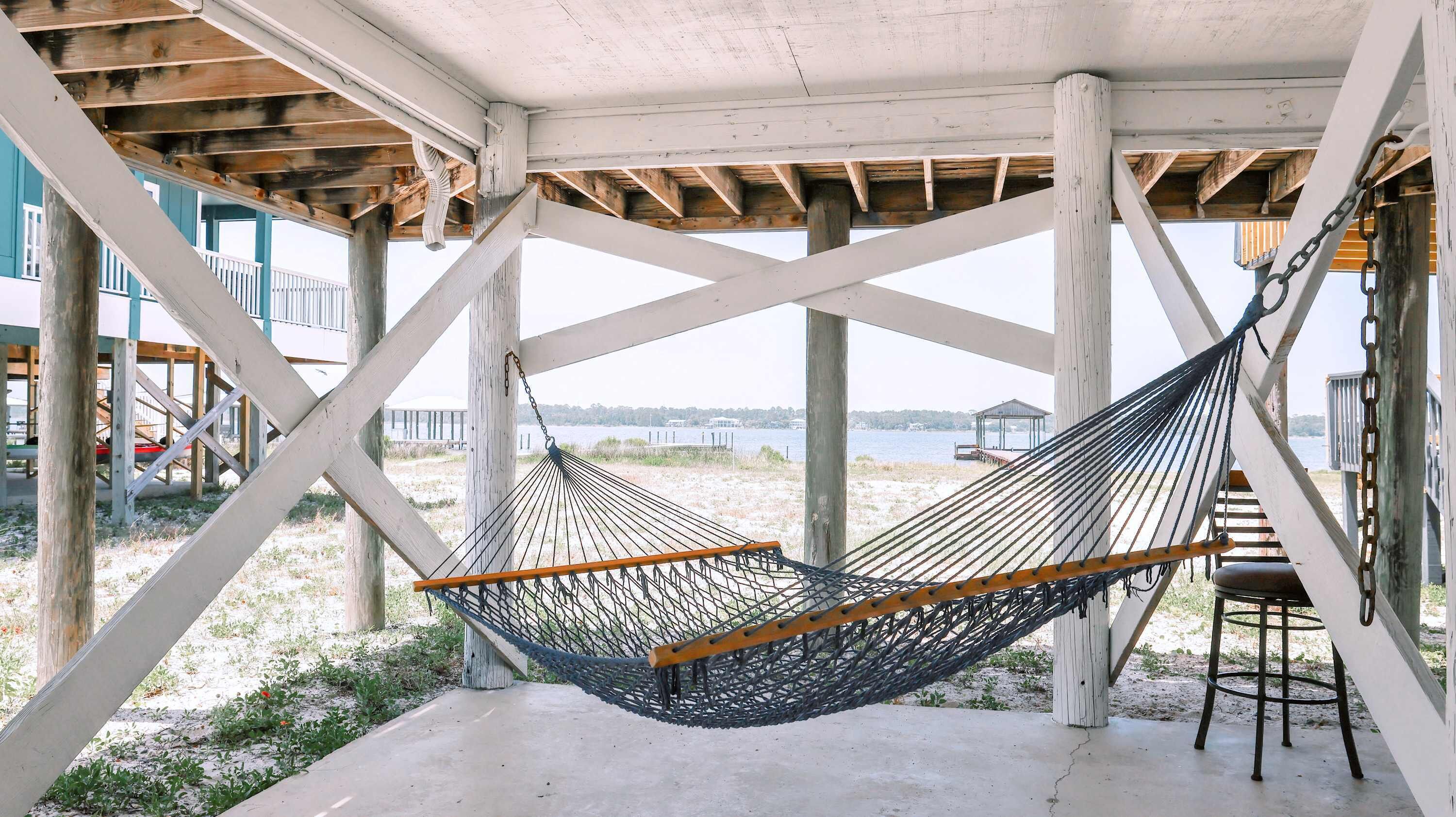 A hammock under a wooden structure with a view of the beach and water.