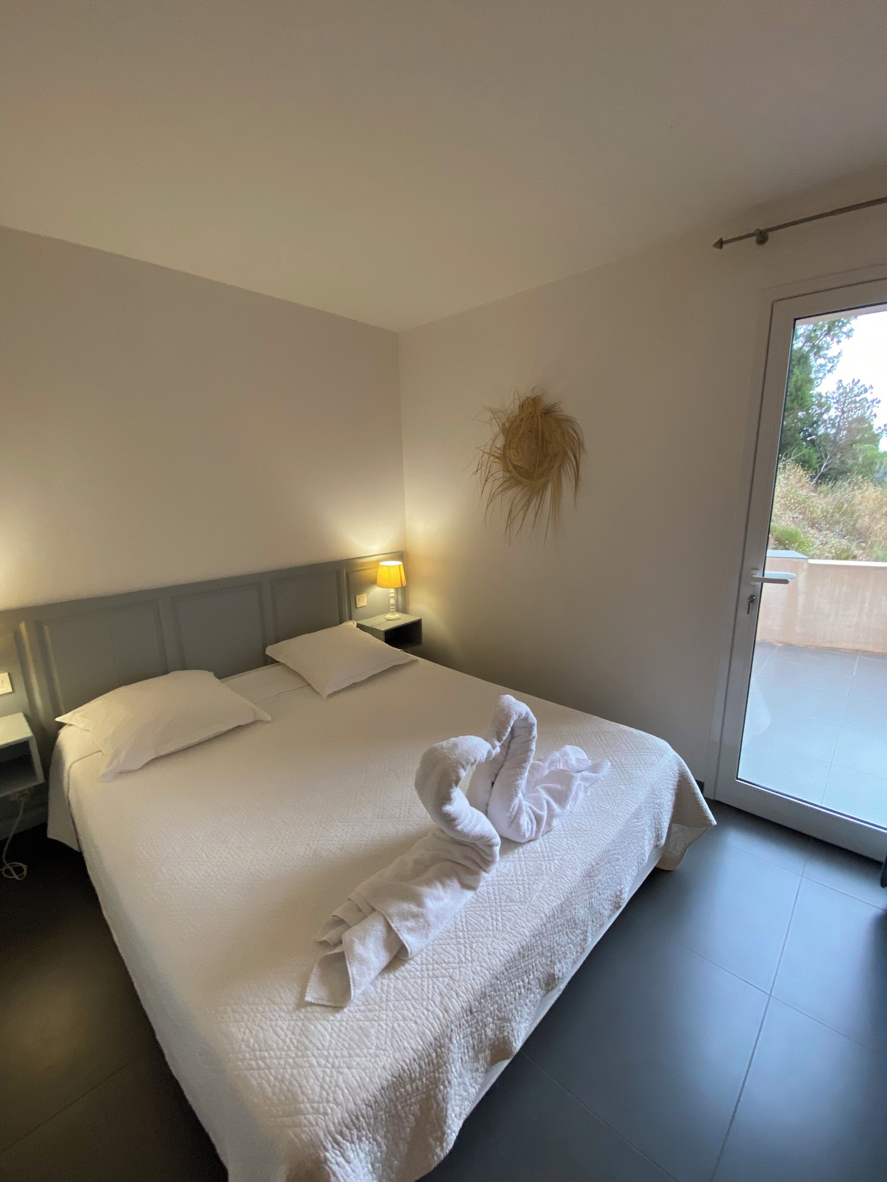 Et hotelværelse med en pænt redt seng, en sengebordlampe, en plante på væggen og en skydedør til et udendørs område.