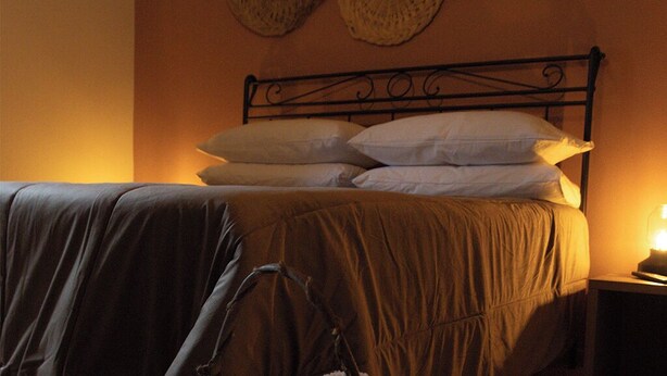 Een bed met een metalen hoofdbord, een bedlampje en wanddecoraties van geweven materiaal.