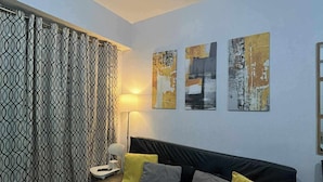 A modern living room with a black leather sofa, patterned curtains, and abstract wall art.