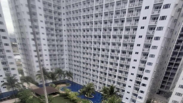 A high-rise residential building with a central swimming pool surrounded by greenery and palm trees.